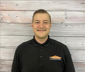 male employee in black smiling in front of wooden background