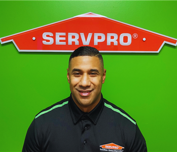 male employee smiling in front of green wall with orange servpro house