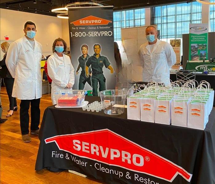 servpro employees in white lab coats standing behind table with black table cloth with servpro logo