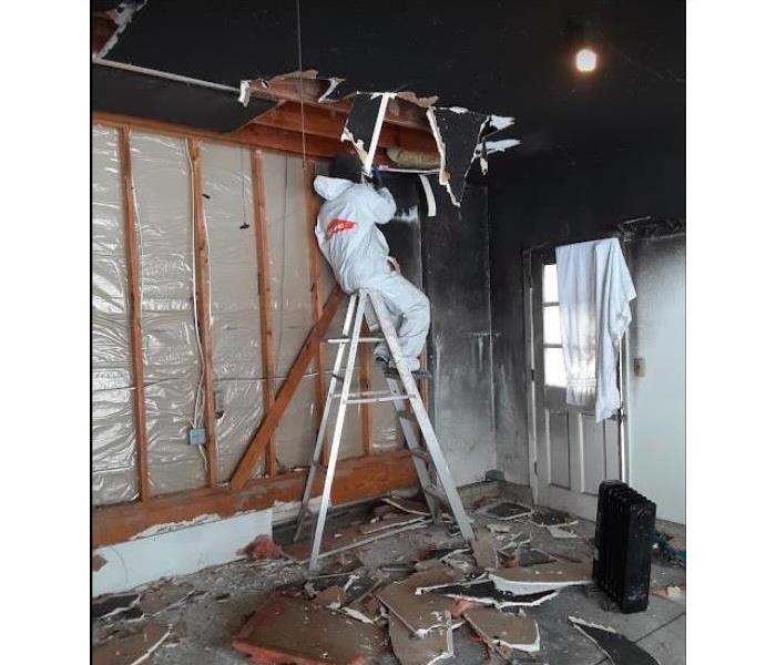 technician in white ppe sitting on ladder doing fire damage restoration